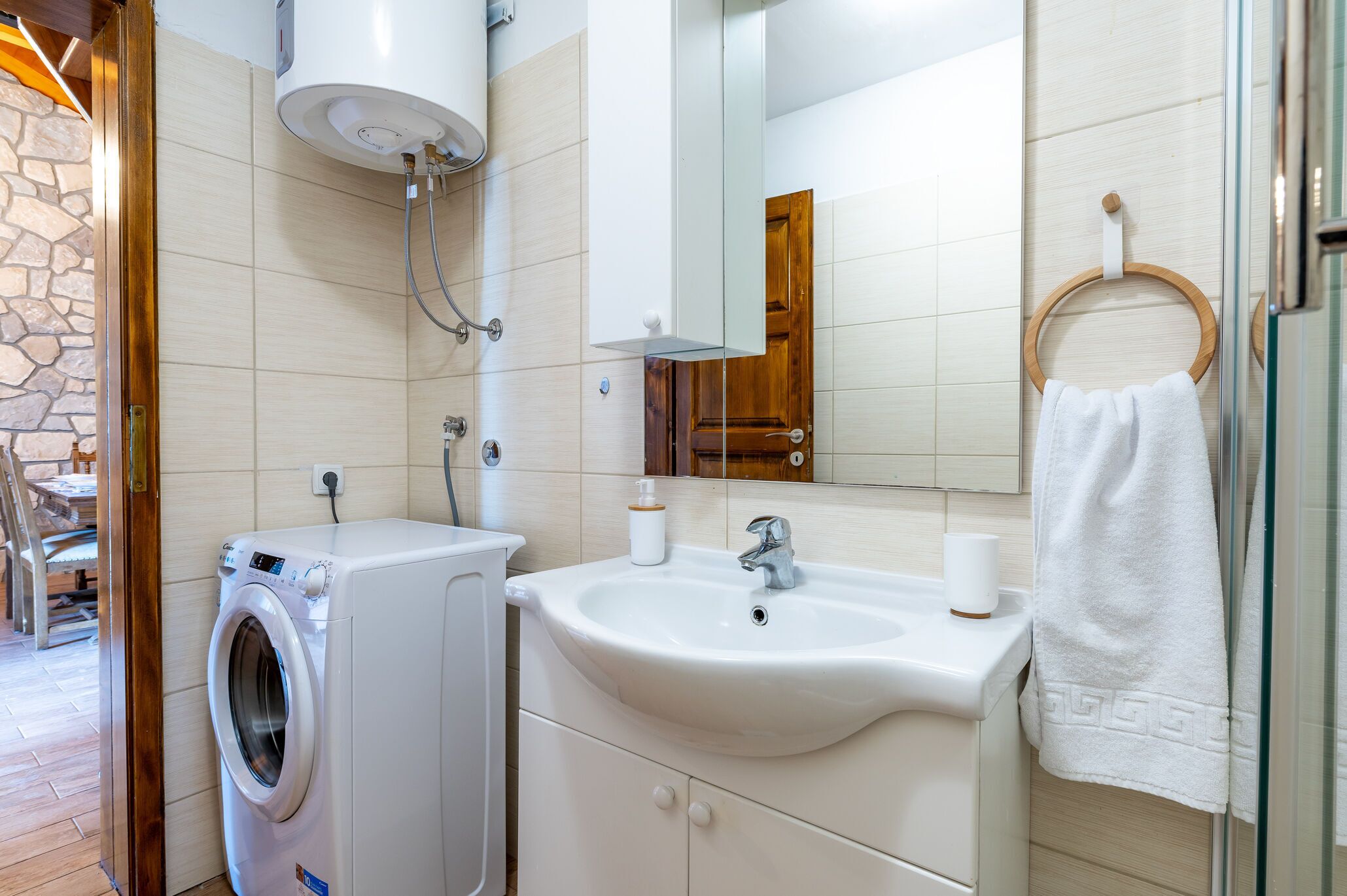 A bathroom with a washing machine, sink, mirror, towel rack, and a stone wall.