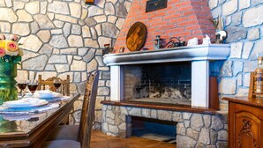 A stone wall with a fireplace, a dining table set with plates and glasses, and a decorative vase with flowers. - Villa Kiara (Unesic)