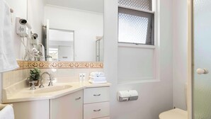 Une salle de bain équipée d’un lavabo, d’un miroir, d’un porte-serviettes et d’une fenêtre avec des stores à motifs.