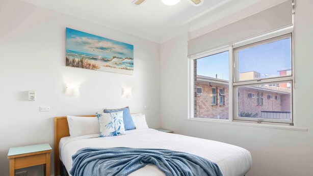 Une chambre à coucher avec un lit, une fenêtre donnant sur des immeubles, un tableau accroché au mur et une table de chevet.