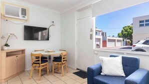 Quarto com mesa de jantar, cadeiras, sofá, televisão e janela com vista para edifícios e um carro.