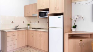 Uma cozinha compacta com armários de madeira, micro-ondas, geladeira, pia e um vaso de planta.