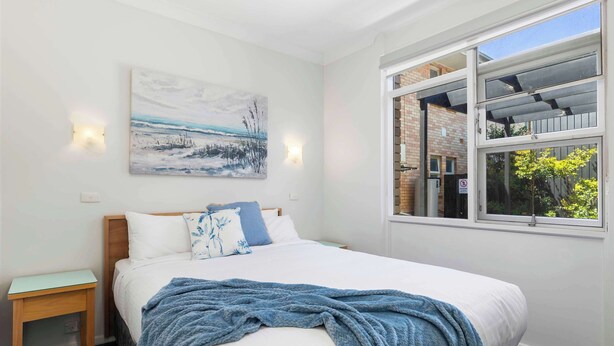 Um quarto com cama, quadro, janela e mesa de cabeceira.