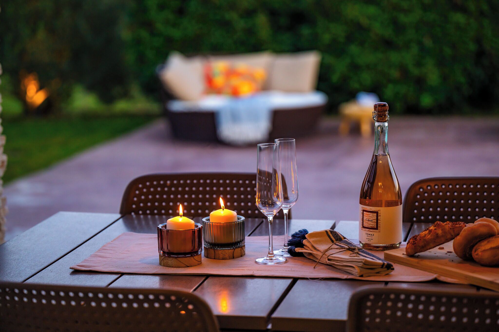 A dining table with candles, glasses, a bottle, and bread.