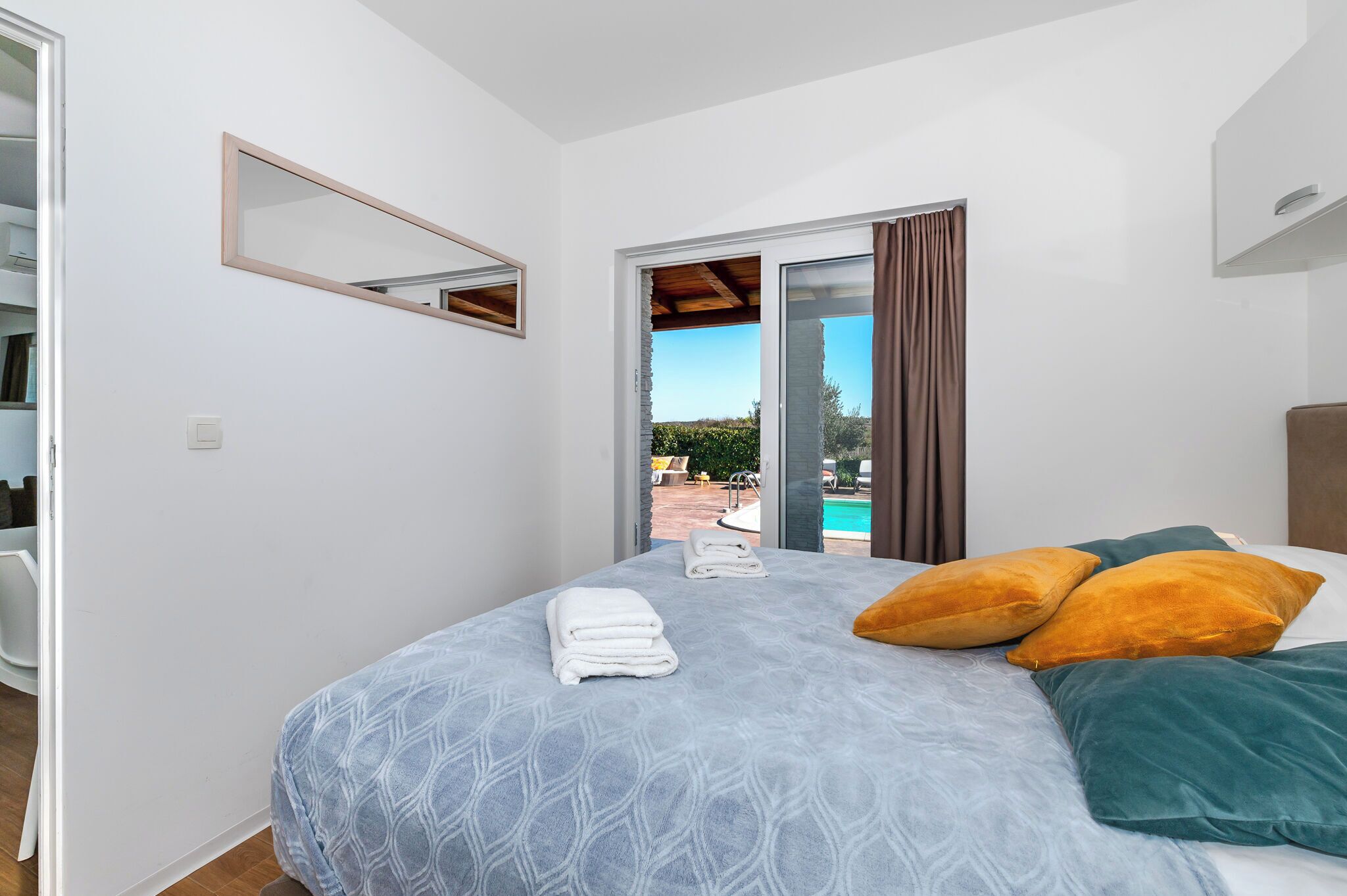 Un dormitorio con cama, ventana con cortinas, vista a una piscina y un espejo en la pared.