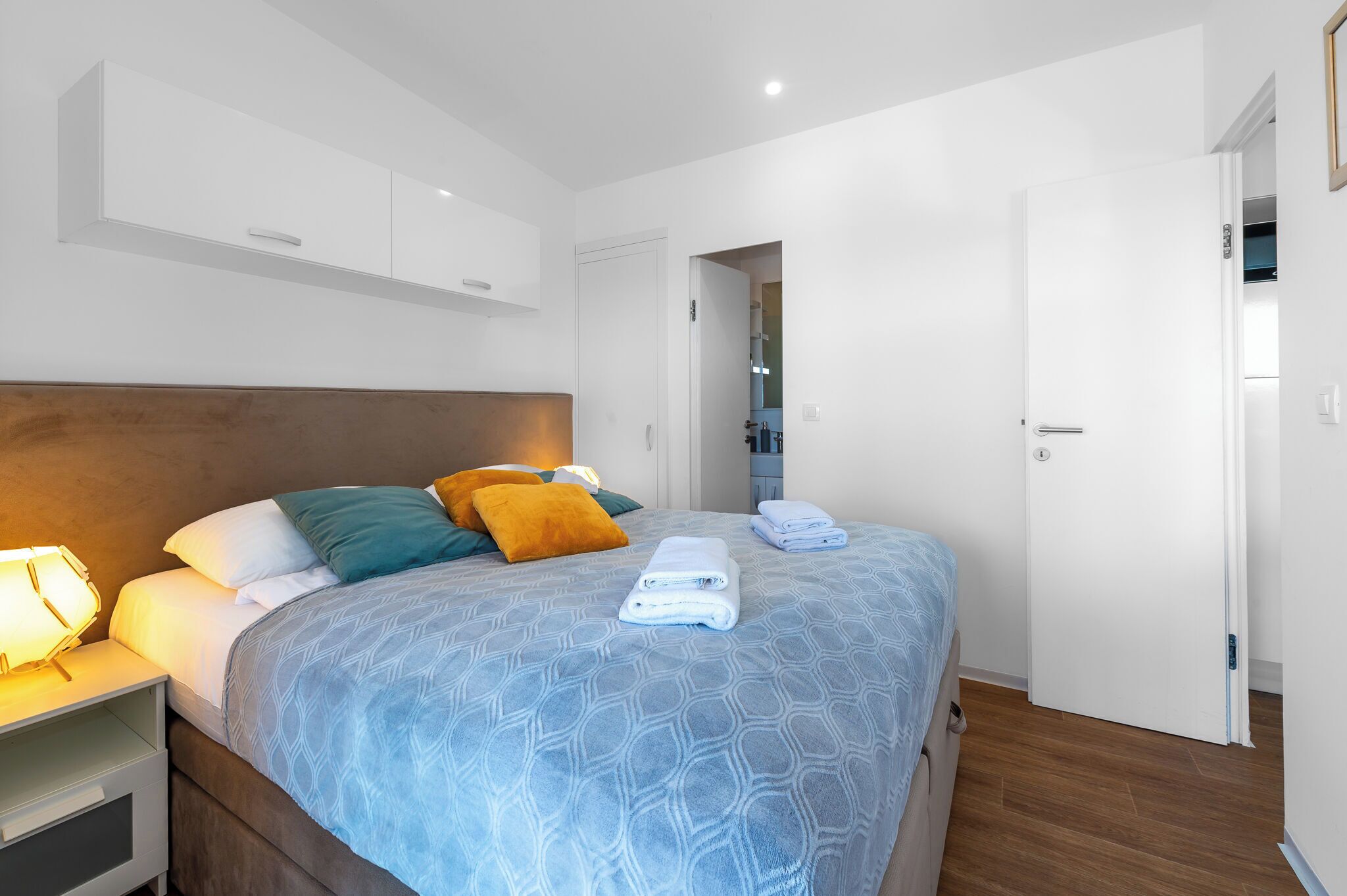 A neatly made bed with a patterned bedspread, a bedside lamp, and a nightstand.