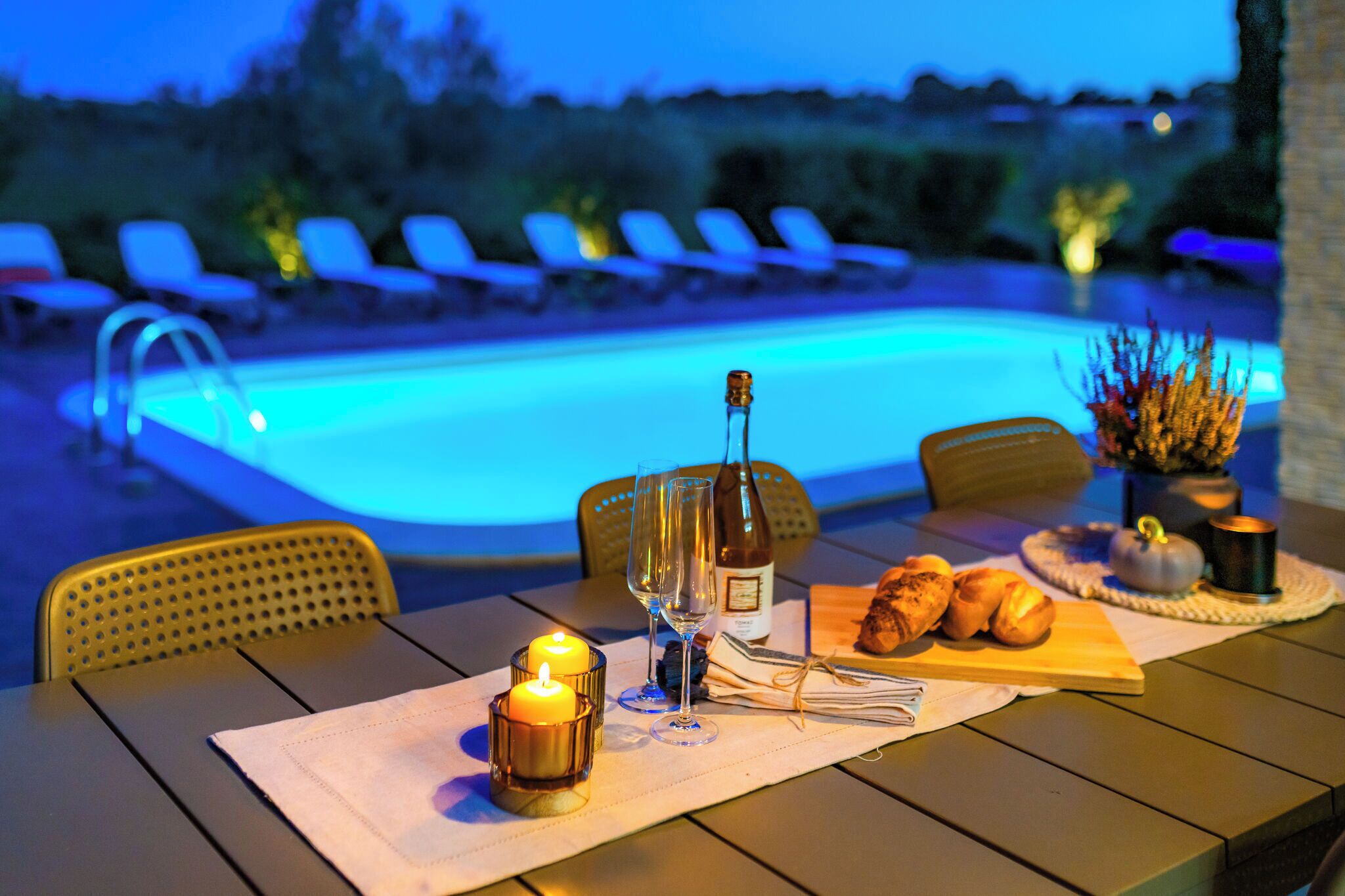 A dining table with a bottle, glasses, candles, and pastries.