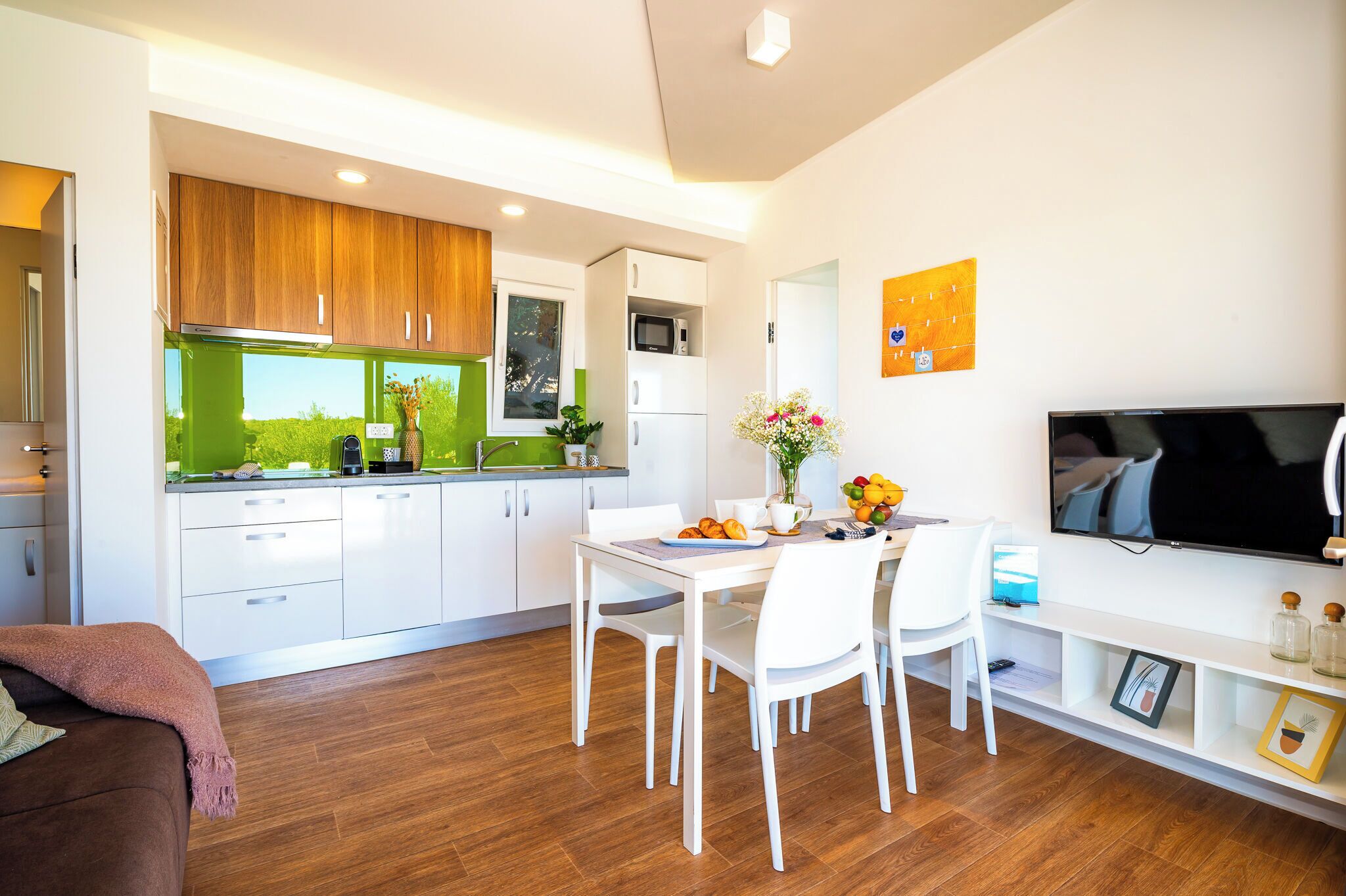 A modern kitchen with white cabinets, a green backsplash, and a dining area with white chairs and a table.
