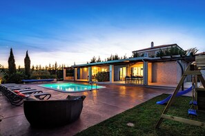 Un jardin avec une piscine, des chaises longues, une balançoire en bois et un espace patio avec une table et des chaises.