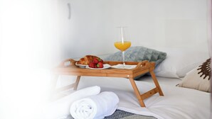 Un lit bien fait, sur lequel repose un plateau en bois contenant un croissant, des fraises et un verre de jus d’orange.