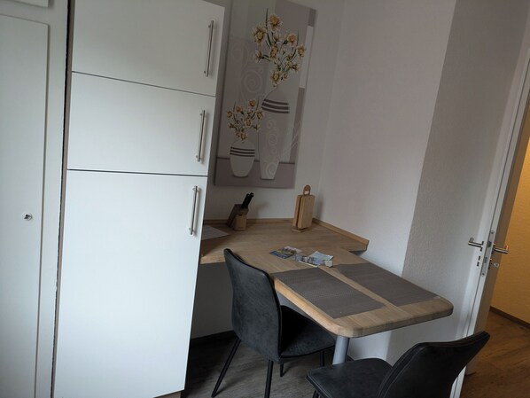 Una kitchenette compacta con armarios blancos, una encimera de madera, dos sillas negras y un juego de cuchillos.
