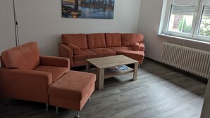 Ein Wohnzimmer mit einer Couch, einem Sessel, einem Couchtisch und einem Stadtbild an der Wand.