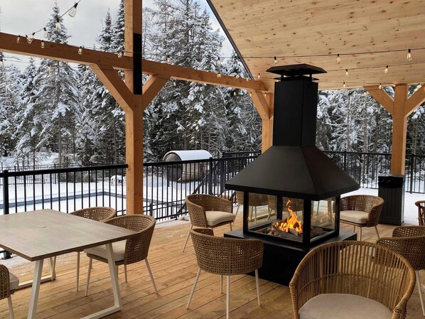 A covered outdoor area with a fireplace, wicker chairs, and a table.