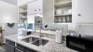 Una cocina moderna con encimeras de granito, lavamanos de acero inoxidable y armarios blancos.