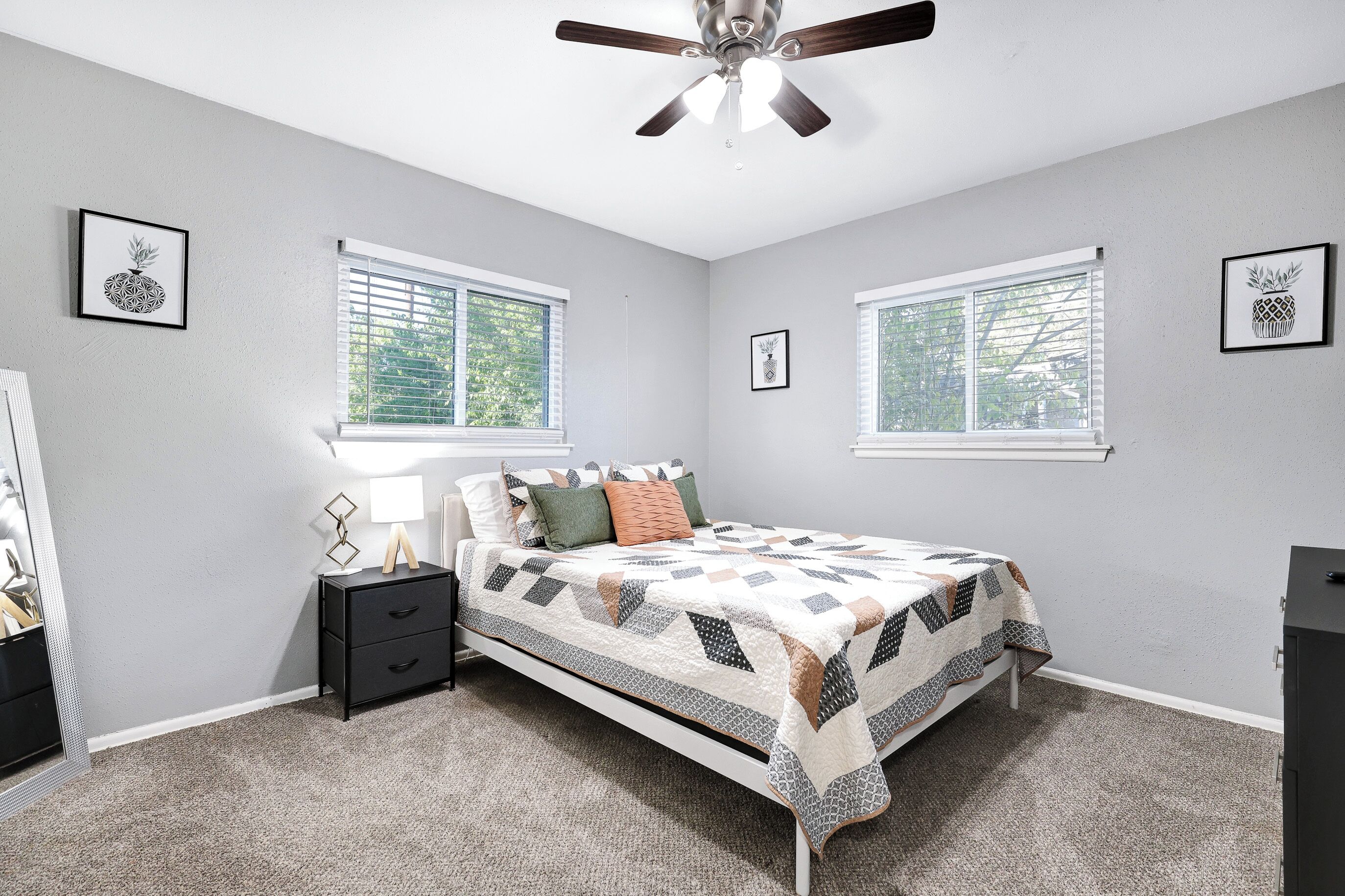 A bedroom with a bed, two windows, a ceiling fan, and a nightstand.