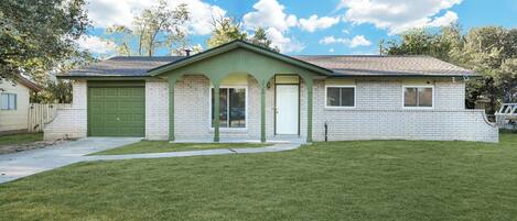 A single-story house with a green garage door, a front porch with a green railing, and a well-maintained lawn.