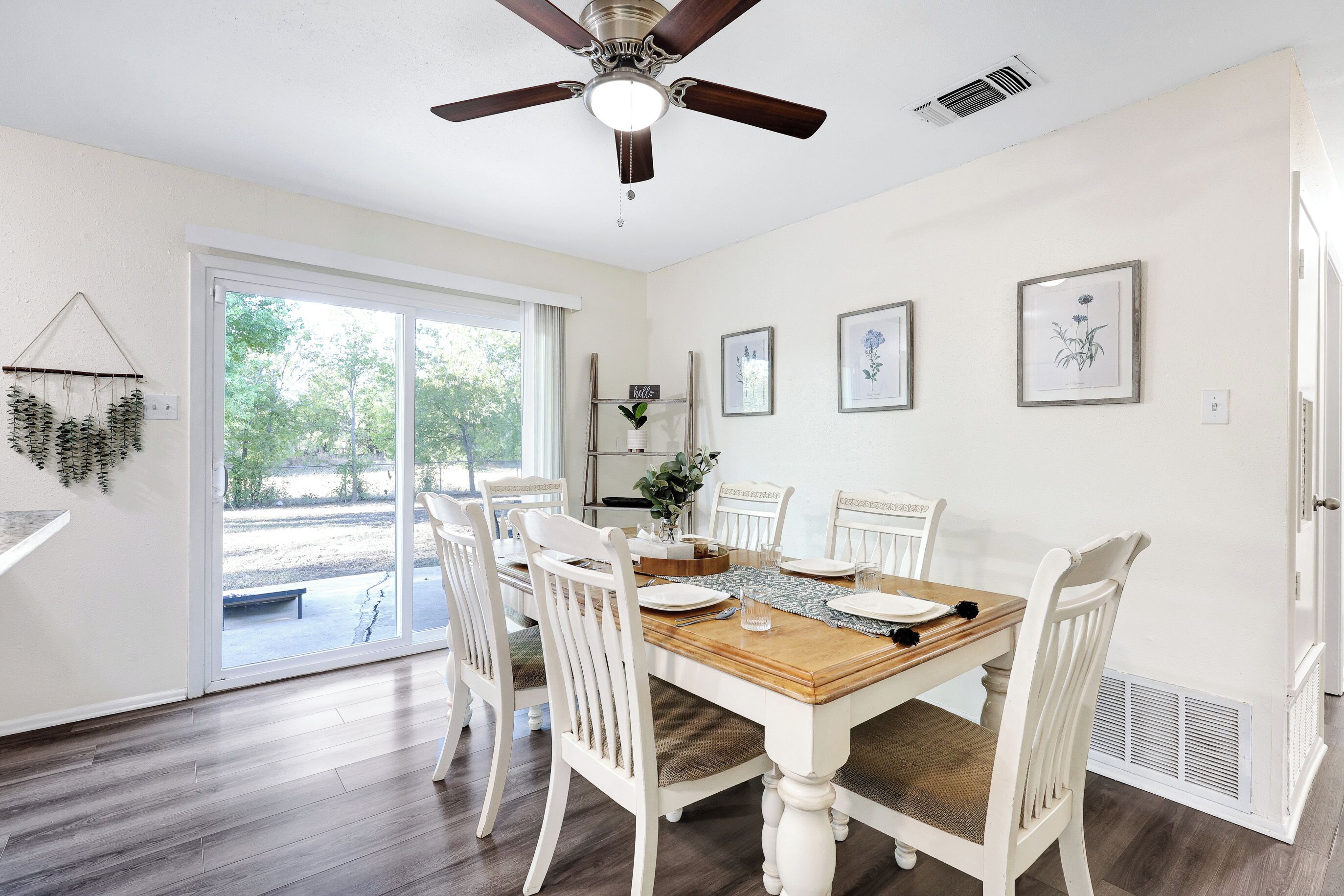 A dining room with a wooden table, white chairs, and a ceiling fan.