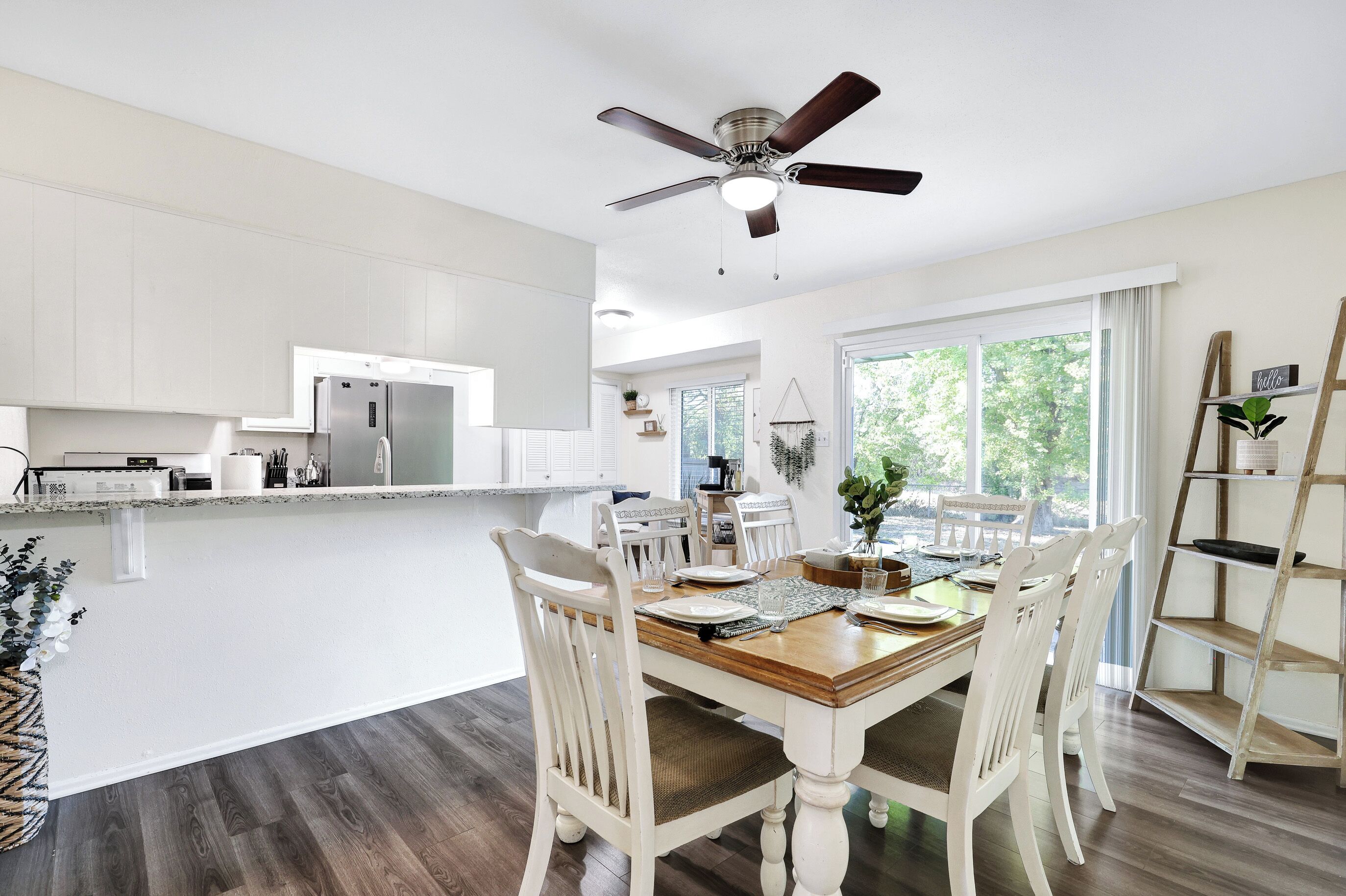 A modern kitchen with white cabinetry, a built-in refrigerator, and a dining area with a wooden table and white chairs.
