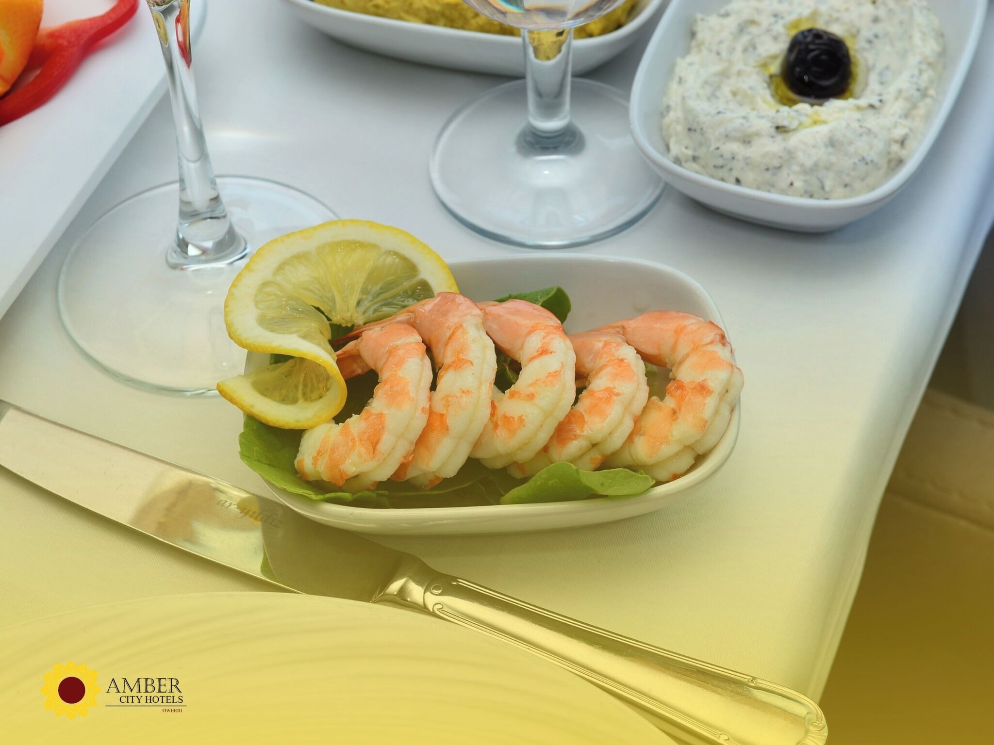 A plate of shrimp with lemon slices and a bowl of dip on a table.