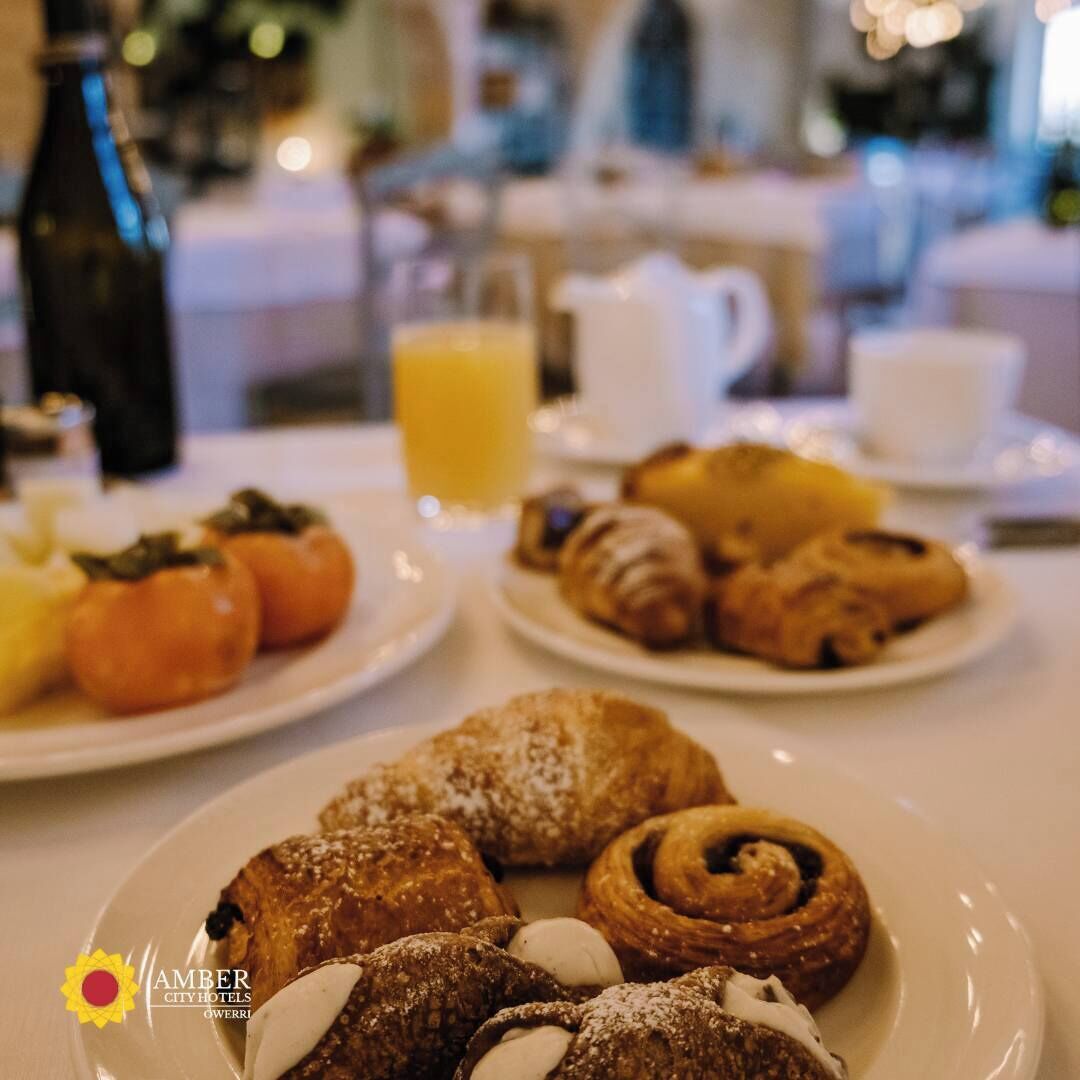 A breakfast setting with plates of pastries, including croissants and cinnamon rolls, and a bottle of orange juice.