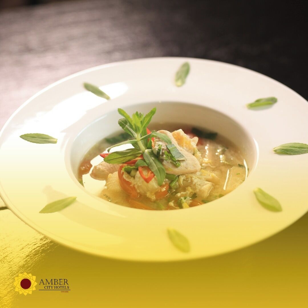 A bowl of soup with a garnish of herbs and vegetables, served on a white plate with a yellow rim.