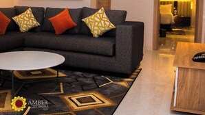 Uma sala de estar moderna com um sofá cinzento, almofadas estampadas, uma mesa de centro redonda e um grande quadro abstrato na parede.