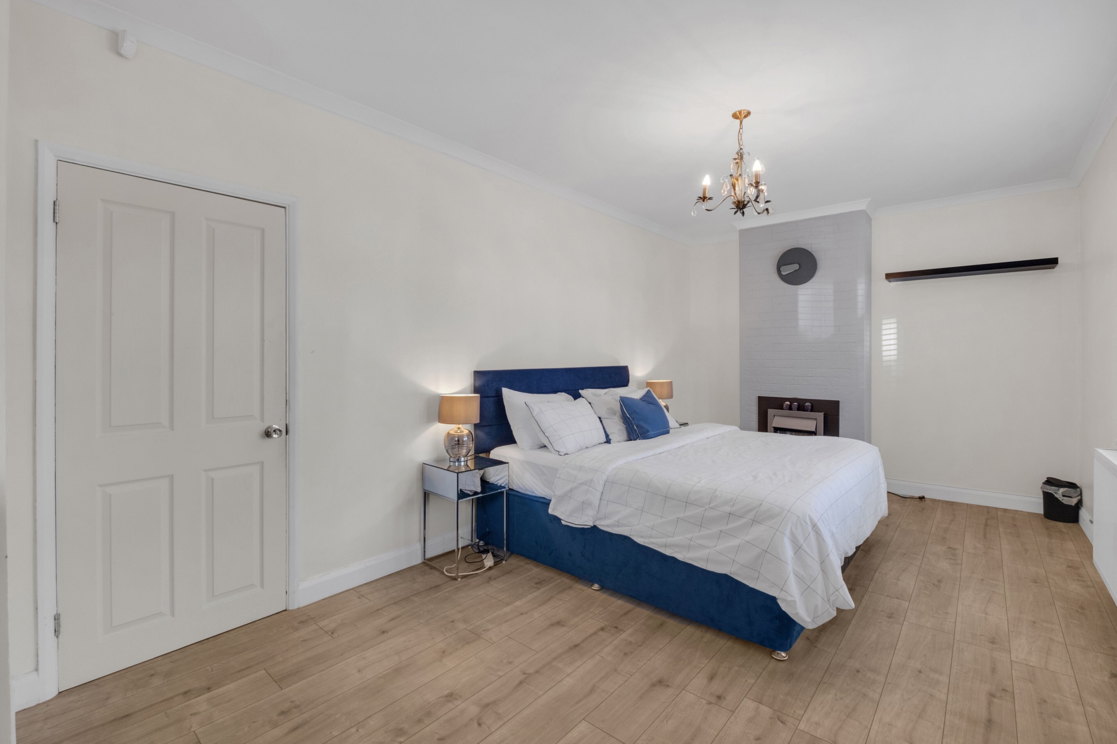 Une chambre à coucher avec un lit, des tables de chevet, un lustre et une porte blanche.