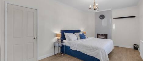 Une chambre à coucher avec un lit, des tables de chevet, un lustre et une porte blanche.
