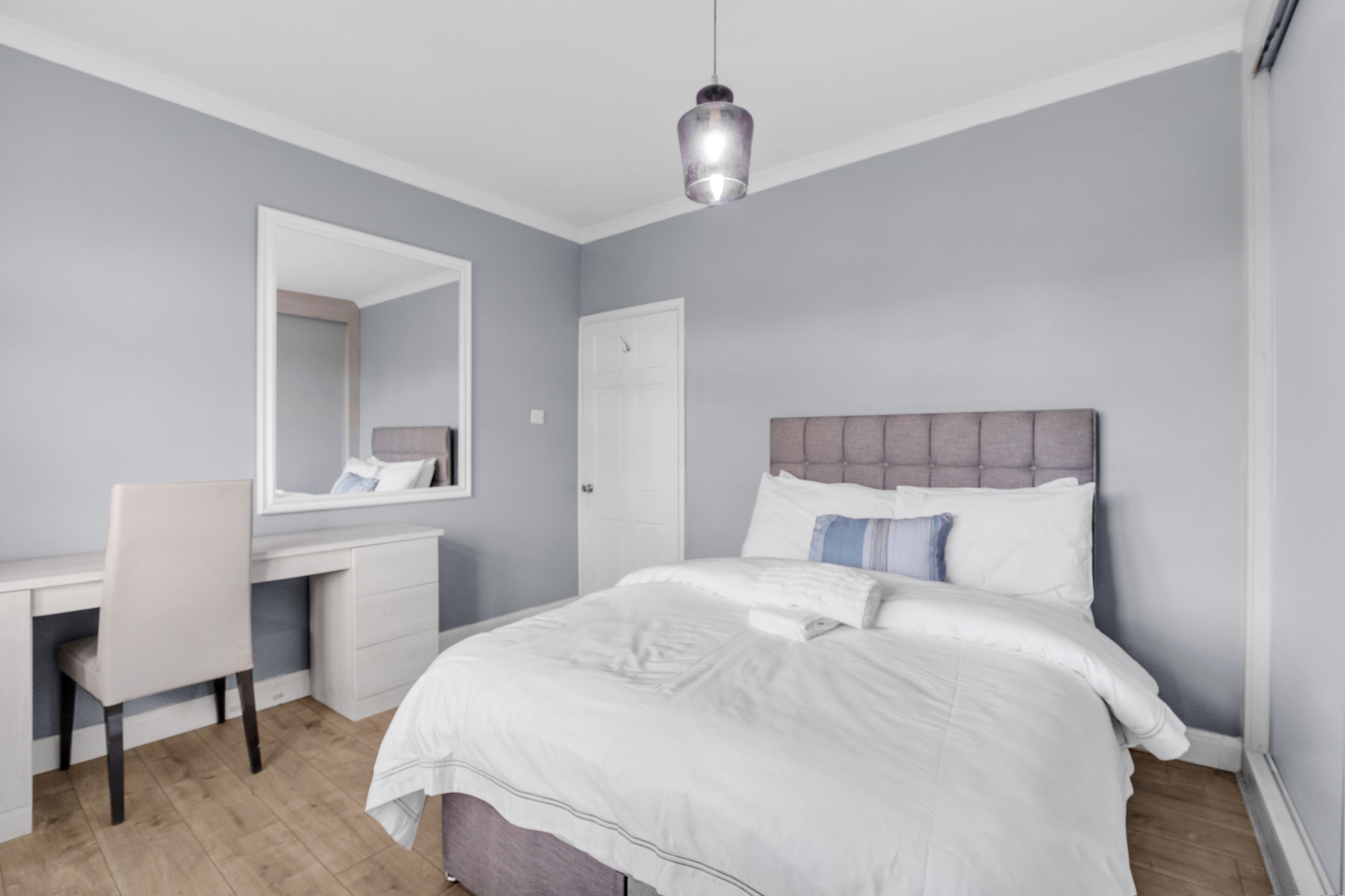 A bedroom with a bed, a desk, a chair, and a hanging light fixture.