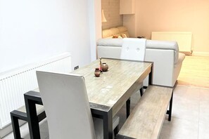 A modern dining area with a wooden table and black chairs, a sofa, and a radiator in the background.