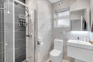 A modern bathroom with a glass-enclosed shower, a toilet, and a vanity with a mirror.