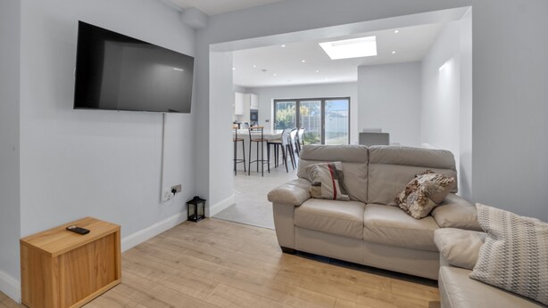 Un salon moderne avec un téléviseur à écran plat fixé au mur, un canapé beige agrémenté de coussins décoratifs et une table d’appoint en bois.