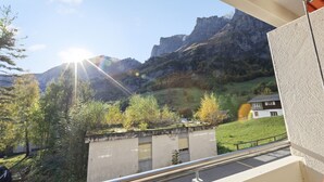 A balcony with a view of a mountainous landscape, a concrete wall, and a building with a sloped roof. - Bright studio with mountain views (Leukerbad)