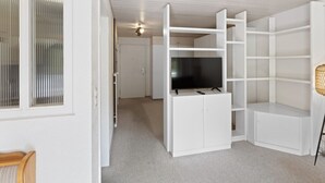 A room with white built-in shelving units, a flat-screen TV, and a wicker chair. - Bright studio with mountain views (Leukerbad)