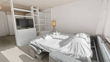 A modern, minimalist hotel room with a bed, a TV, a desk, and a lamp.
