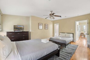 Quarto com duas camas, um ventilador de teto, cômoda e televisão.