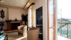 A living room with a fireplace, a sofa, a round table, and a balcony with a view of boats. - Apartment Il Veliero with Amazing Sea View (Portoferraio)