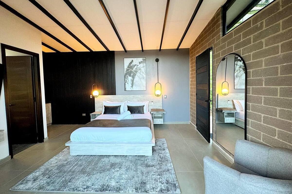A modern bedroom with a large bed, bedside tables, a mirror, and a view of the outside.