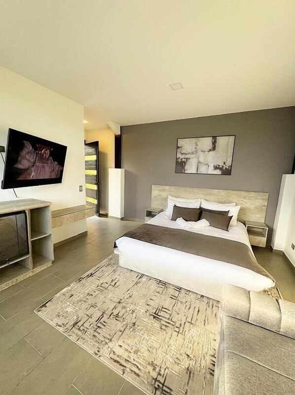 A modern bedroom with a large bed, a flat-screen TV, and a minimalist decor. - Rooca Guatape (El Peñol)