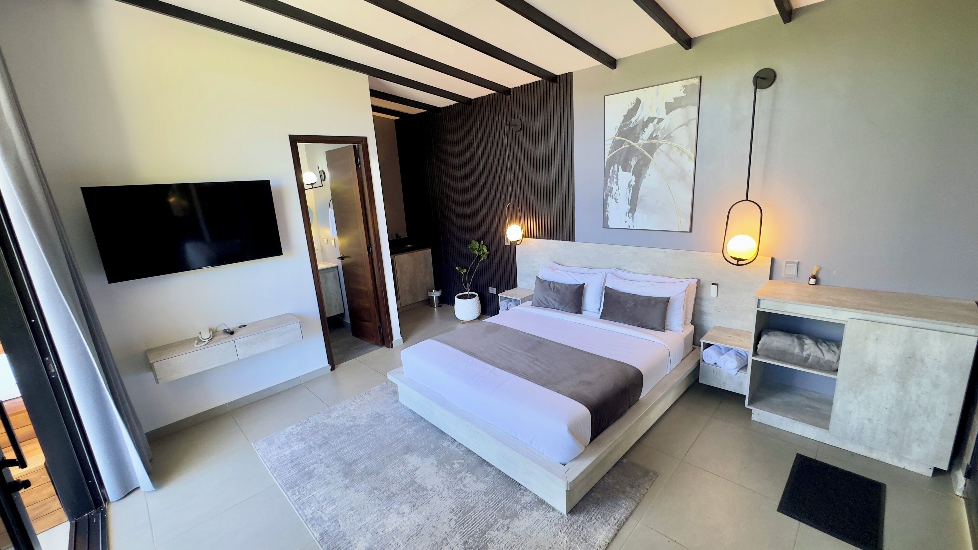 Ein modernes Schlafzimmer mit einem großen Bett, Nachttischen, einem Fernseher und einer Wandleuchte.
