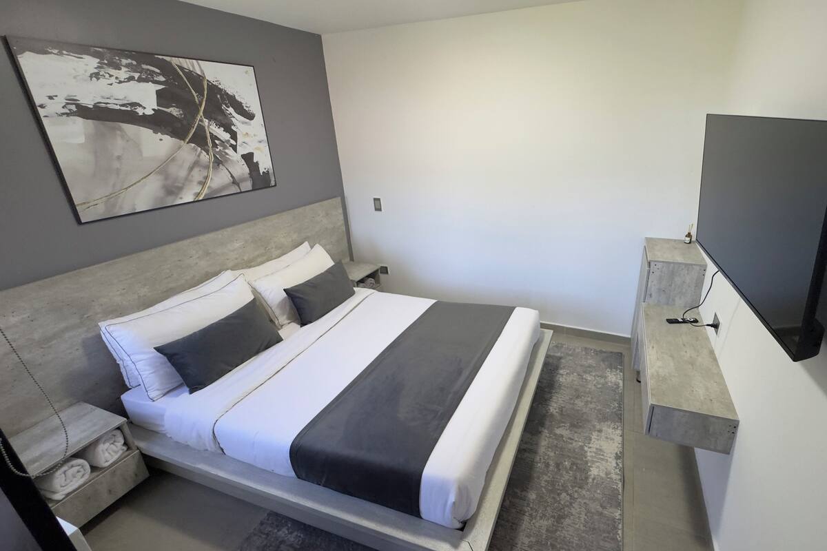 A modern hotel room with a bed, bedside tables, a flat-screen TV, and a painting on the wall.