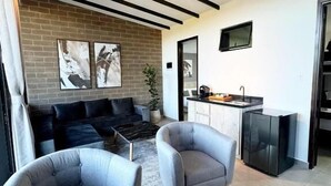 A modern living room with a sofa, two armchairs, a coffee table, and a fireplace. There is a kitchen area with a refrigerator and a TV mounted on the wall. - Rooca Guatape (El Peñol)