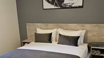 Une chambre moderne avec un grand lit, une tête de lit, une table de chevet et une œuvre d’art accrochée au mur.
