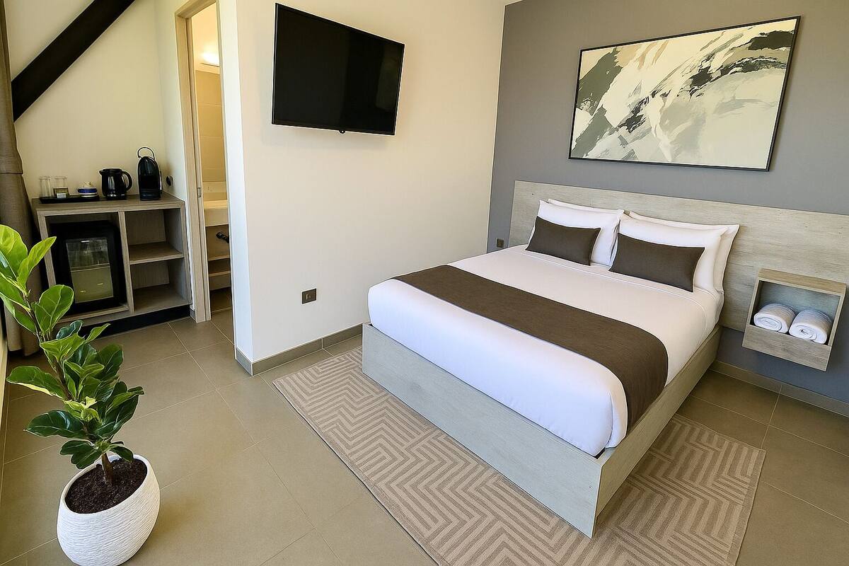 A modern hotel room with a large bed, a flat-screen TV, a painting on the wall, and a small plant.