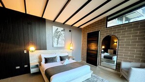 A modern bedroom with a large bed, a nightstand, a mirror, and a seating area. - Rooca Guatape (El Peñol)
