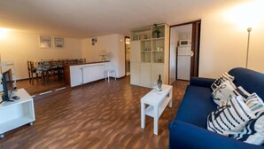 Una sala de estar con un sofá azul, una mesa de centro blanca y una zona de comedor con sillas y una mesa de madera.