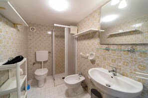 A bathroom with a toilet, bidet, and sink, a shower area, and a mirror with shelves. - Apartment I Pini with a view of the gulf (Portoferraio)