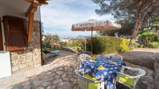 Un patio de piedra con una mesa, sillas y una sombrilla, con vistas al campo.