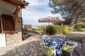 A stone patio with a table and chairs, an umbrella, and a view of the countryside. - Apartment I Pini with a view of the gulf (Portoferraio)