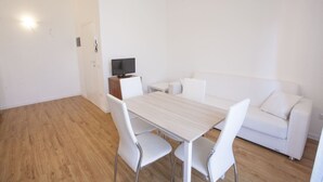 A modern, minimalist living room with a wooden floor, white furniture, and a flat-screen TV on a wooden stand. - Anna Apartment just a few minutes from the centre (Portoferraio)